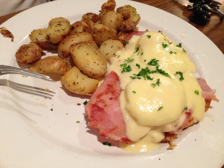 a plate topped with cheese and ham covered in gravy next to potatoes