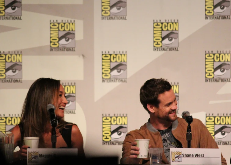 a man and woman sitting at a table with microphones in front of them