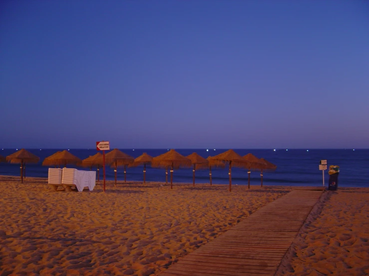 sandy beach area with lawn chairs, thatched umbrellas, and sign that says don't enter on it