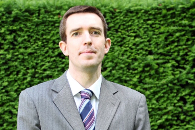 a man with a suit and tie posing in front of a hedge