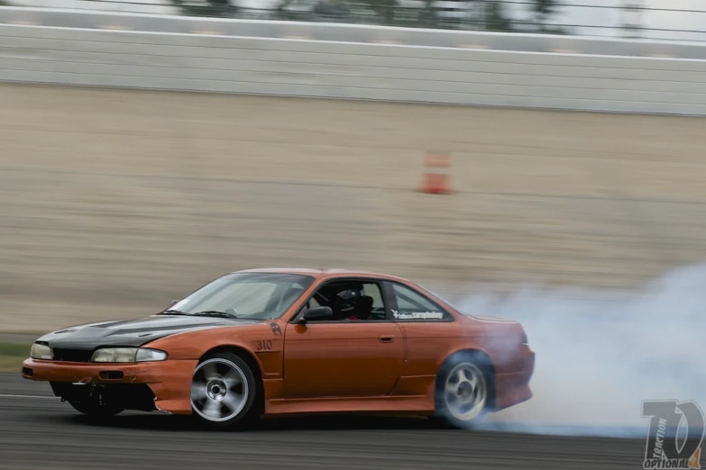 an orange car rolling around a track while the smoke is billowing
