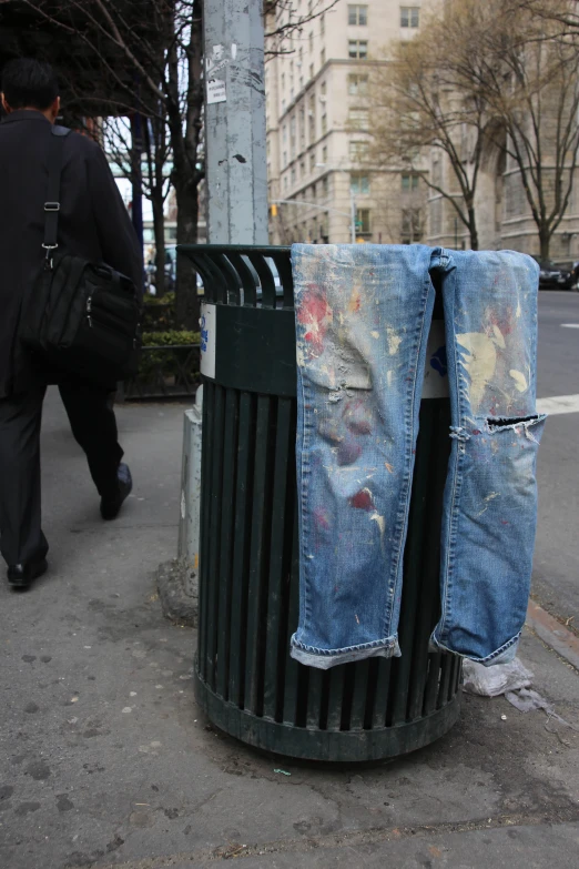 a man walking past a garbage can with his jeans ripped off