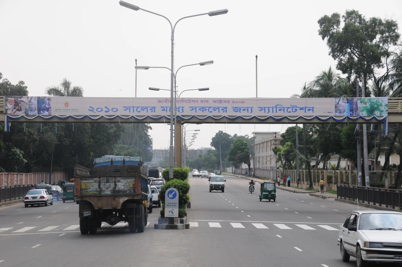 the city street has cars driving under a large banner