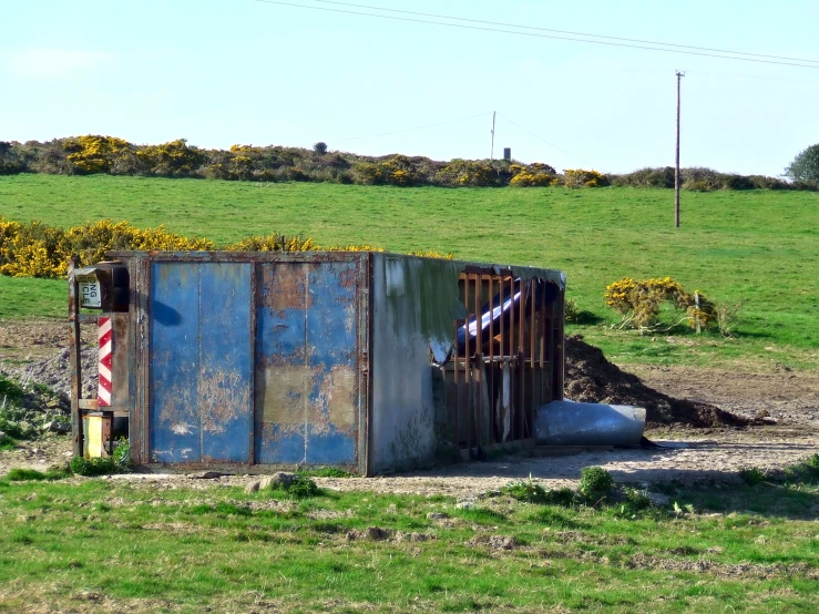 a rusted, metal building near a field with some bushes