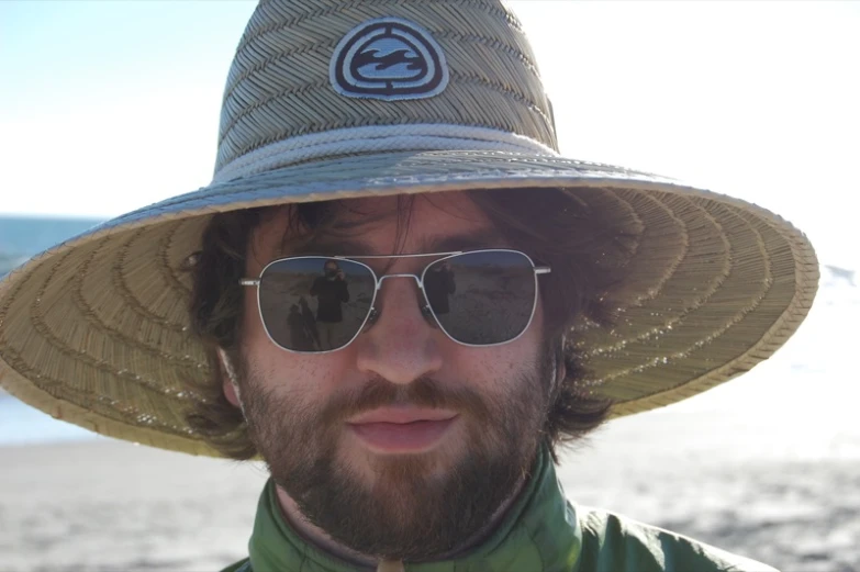 a man with a hat and sunglasses standing in front of the water