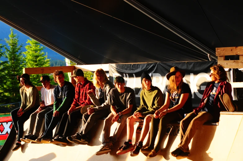 several people with hats sitting and standing on a skateboard ramp