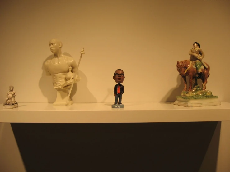 three statues of men are displayed on a shelf