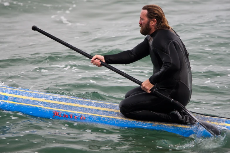 a man in a wetsuit rowing on his surfboard