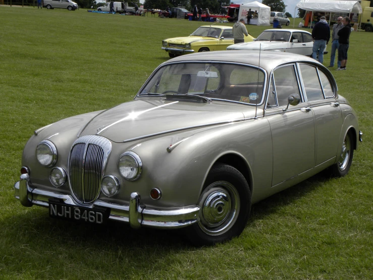 a silver classic car parked on top of a grass covered field