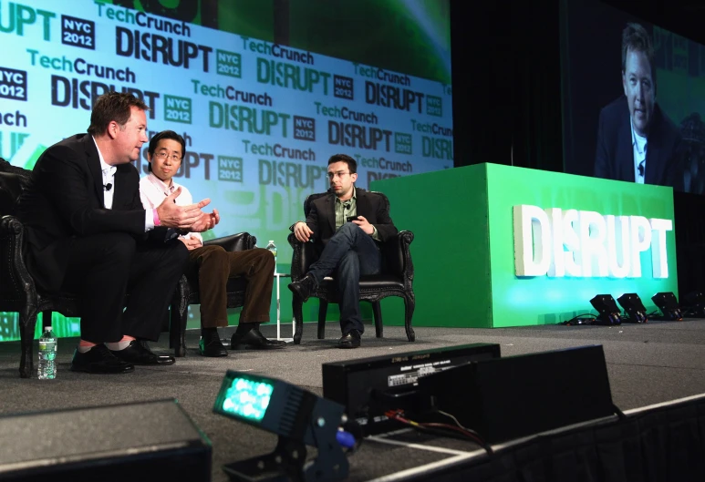 three men on stage and one is sitting