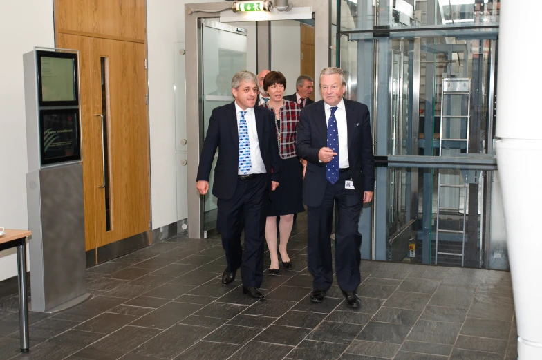 two men and a woman walk past an elevator