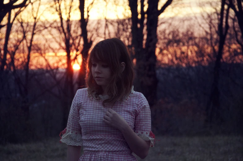 a girl wearing a pink dress standing in the grass with trees