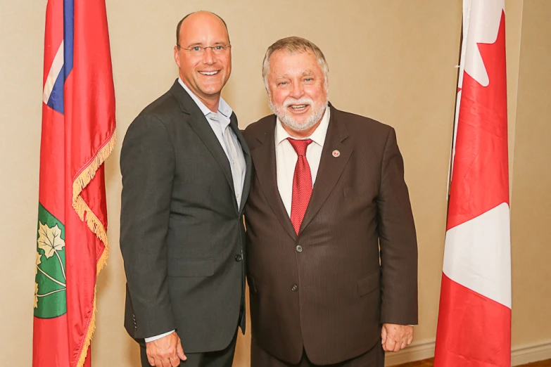 two men in suits posing in front of flags