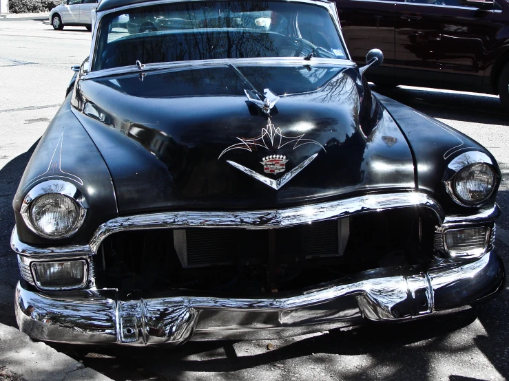 a black classic car with chrome spokes on the hood