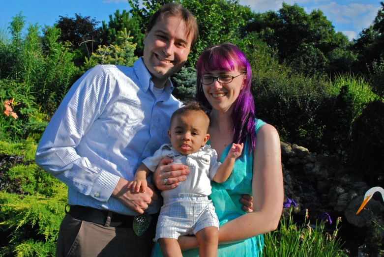 a young family poses for a picture in front of plants