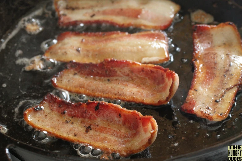 bacon frying in oil and being seasoned in set