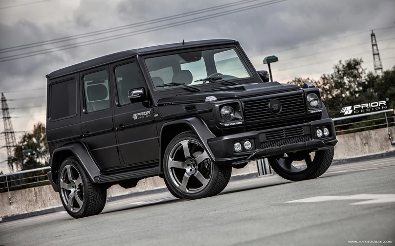 a black mercedes benz benz benz g63 in front of a fence and cloudy sky