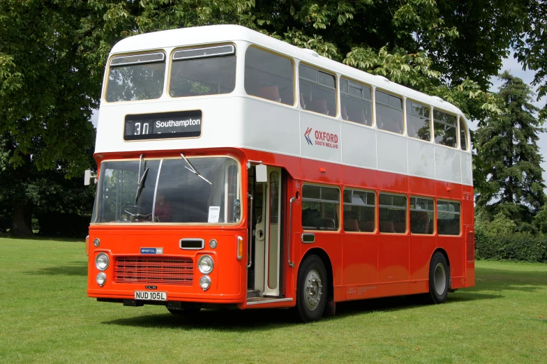 the red and white double decker bus is parked on the grass
