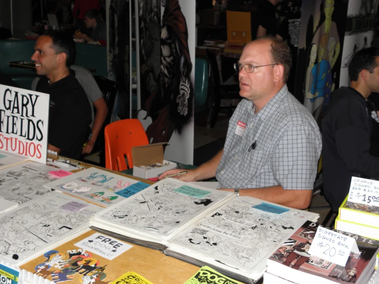 two men at a book signing table with art on it