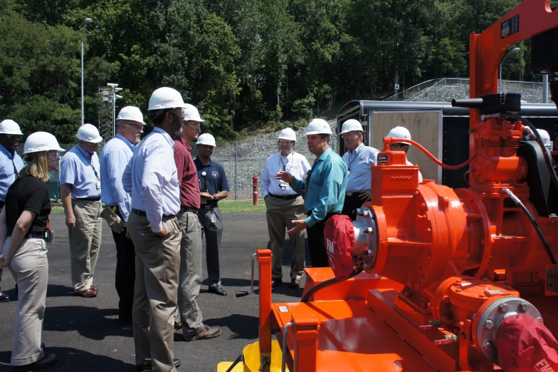 men in hard hats are talking next to orange pipes