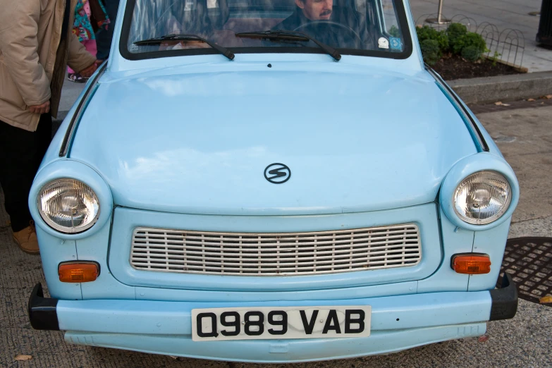 a small blue car with a man driving in the passenger seat