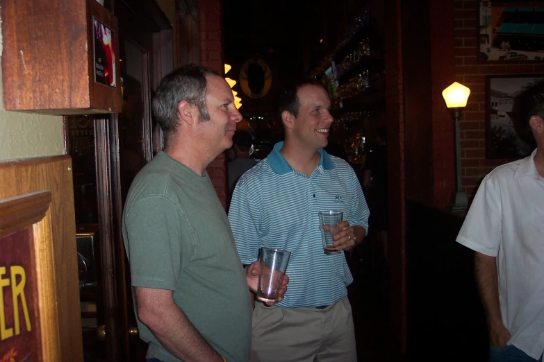 two men laughing at each other while holding glasses