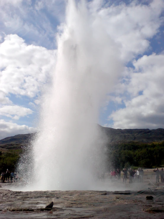 people gather around the geyser as it pours water into the air