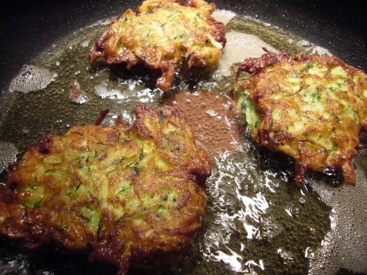 four burger patties in frying pan with oil