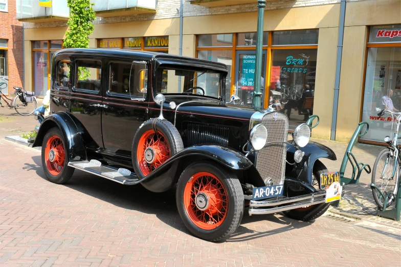 an old black car with bright orange wheels and rims parked on a street