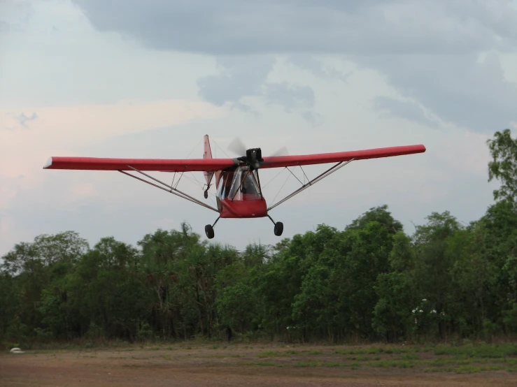 a small red plane flying over a lush green forest