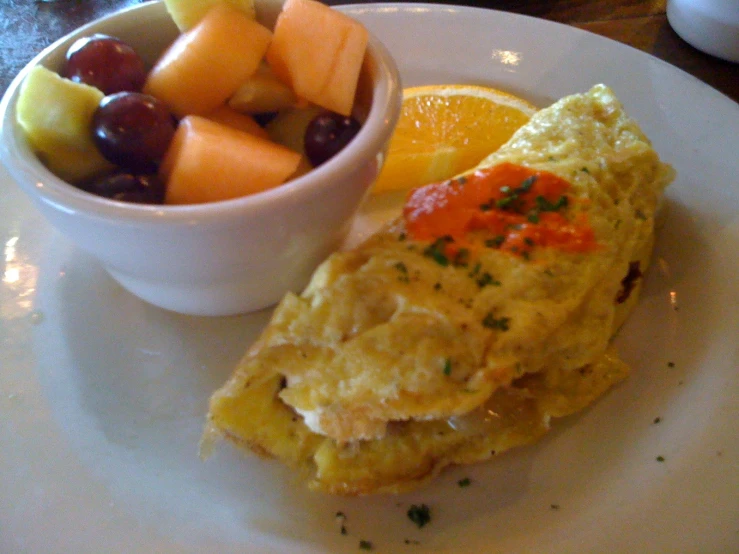an omelet sitting on a white plate next to a bowl of fruit