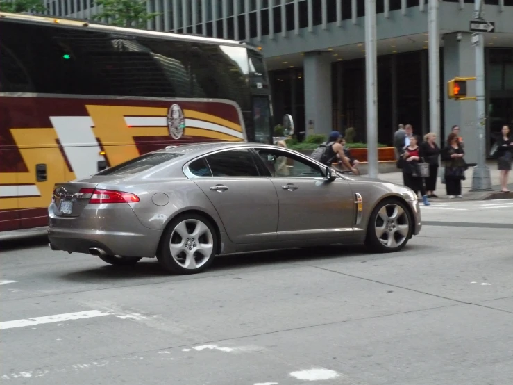 a gray car stopped at an intersection while a bus passes by