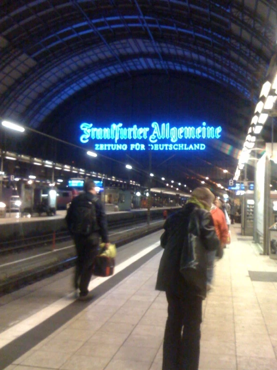 a train station with people on the platform and signs above