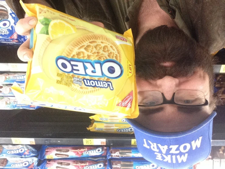 a bearded man in a baseball cap holding up a bag of oreo chips