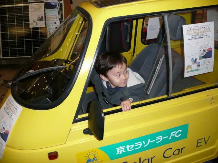 small child sits inside a yellow car looking out the window