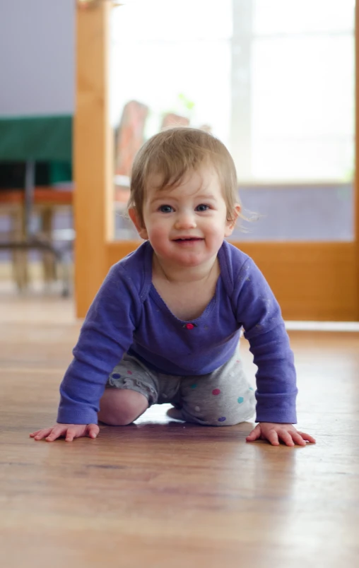 the smiling toddler is crawling on the floor