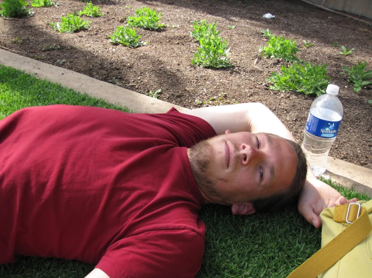 a man laying on the grass with a bottle and water