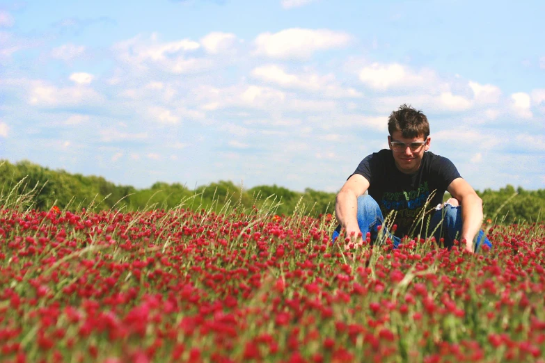 a young man is crouched in the middle of a flower field