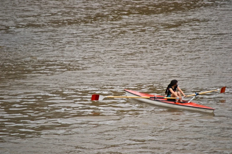 a woman paddles a red kayak through water