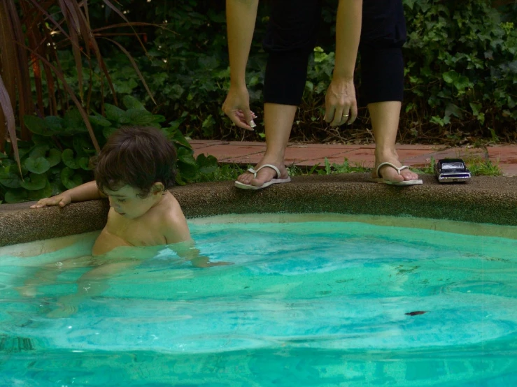 a young child is in a pool of water while an adult watches