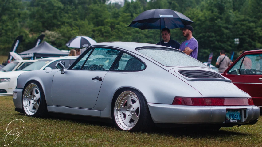 a porsche in the rain with a man under an umbrella standing next to it