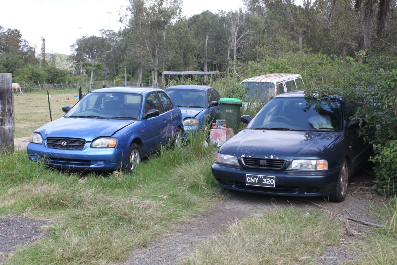 several abandoned cars parked in the weeds next to a wooded area