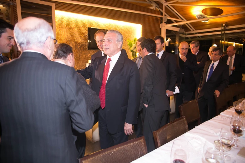 several men in suits and ties having conversation in a large room