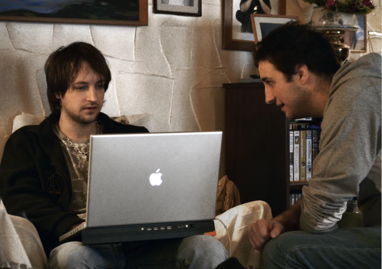 two men in a room with a laptop and a book shelf