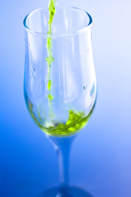 a wine glass with a green liquid pours into it