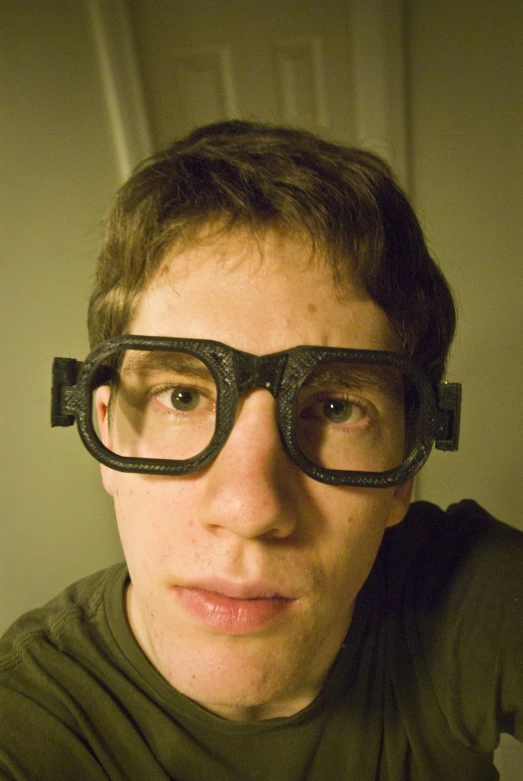 young man wearing glasses standing in front of a wall