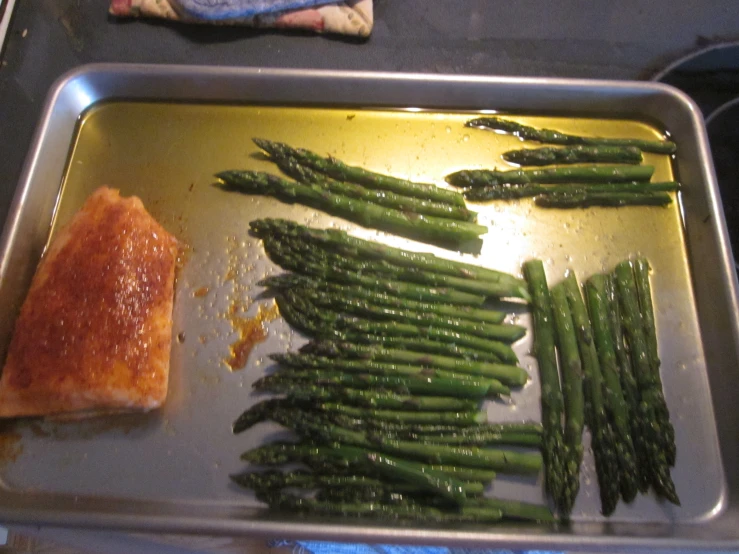 asparagus and cheese are on a baking pan next to a piece of fish