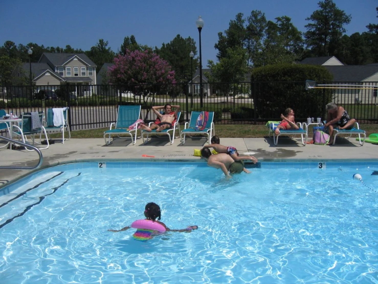 people are playing in the swimming pool with chairs and lawn furniture