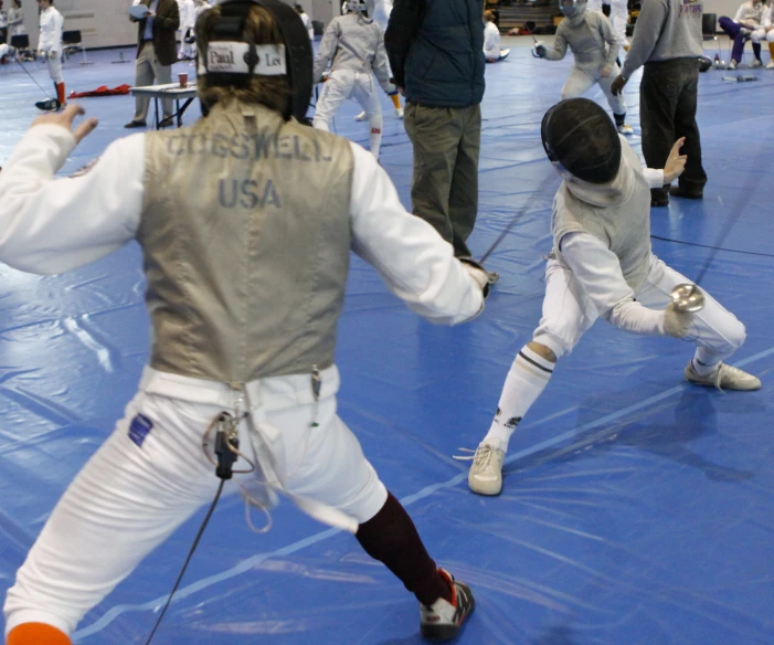 two people wearing fencing suits on a blue floor