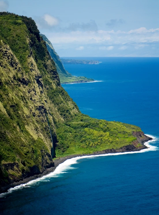 the coast of a green island with white waves crashing over it